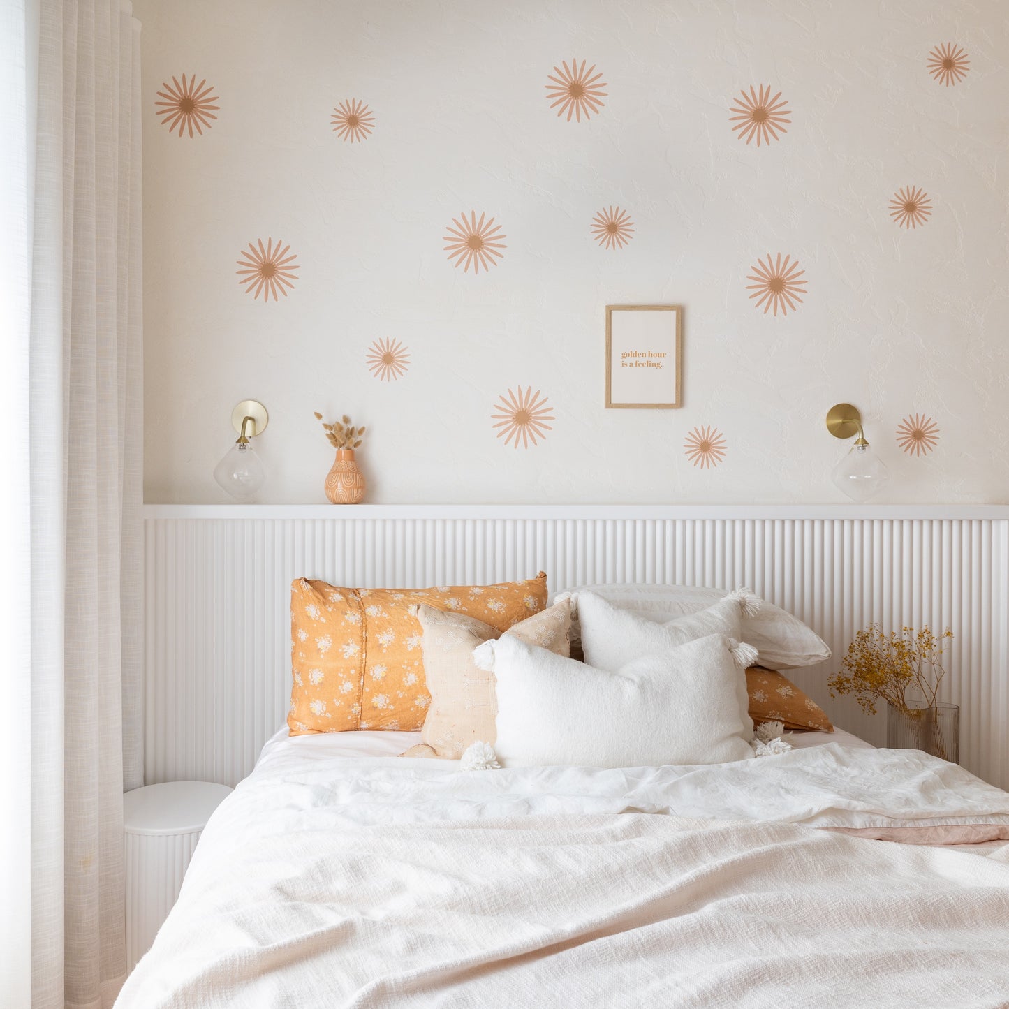 Neatly made bed with decorative pillows against a wall with sunflower decals.