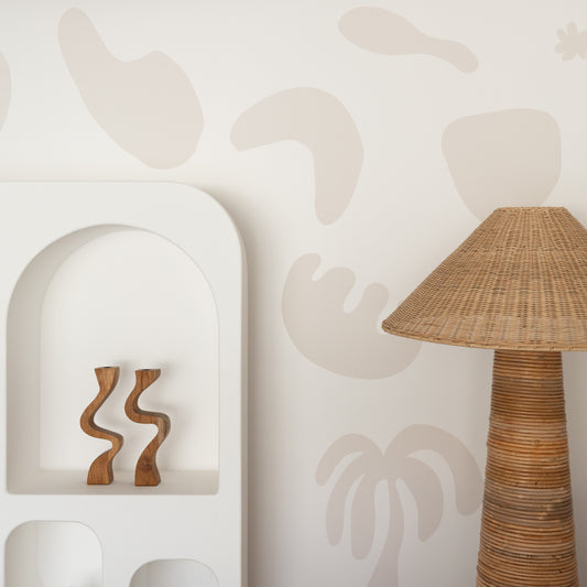Decorative wall with abstract shapes, a shelf with wooden candle holders, and a rattan lamp.